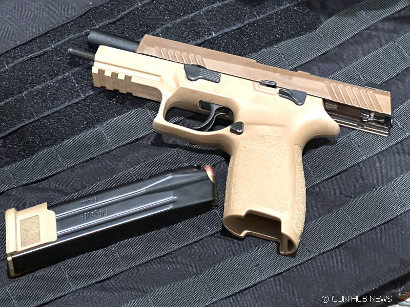 A tan M17 pistol on a black cloth wiht the magazine laying beside it. 