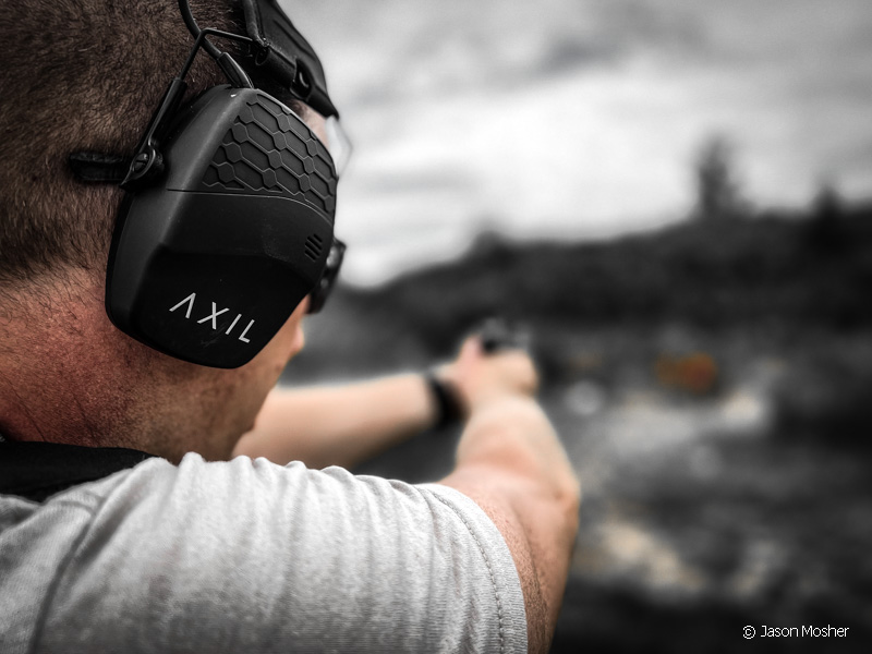 A person shooting with a pair of black earmuffs on.